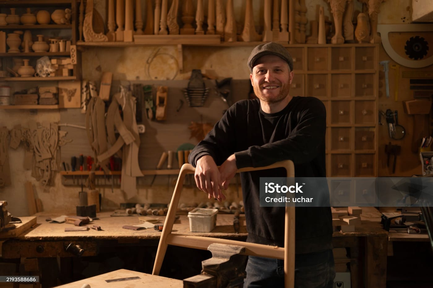 Ébéniste appuyé sur une chaise qu'il vient de terminer dans son atelier