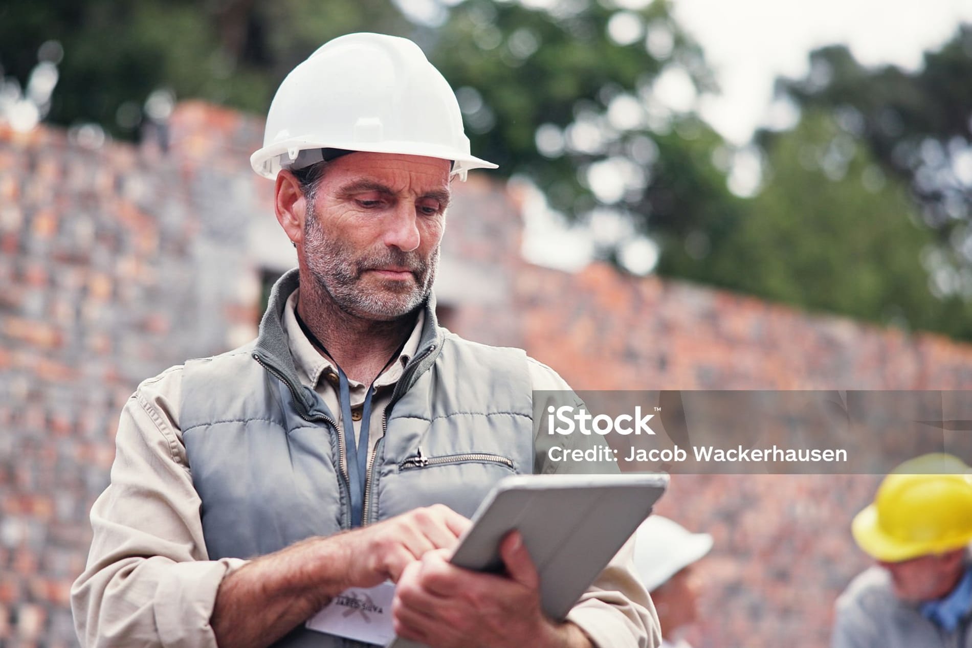 Chef de chantier consultant un devis sur sa tablette devant un bâtiment en construction